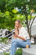 © StockPhotoRepublic - Caucasian Woman Sitting and Using Phone While Having a Cup of Coffee Outdoor a Park