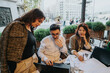 © qunica.com - A multicultural group of business people brainstorming ideas at an outdoor cafe. The diverse team is engaged, analyzing documents, and collaborating on a project, fostering creativity and teamwork in