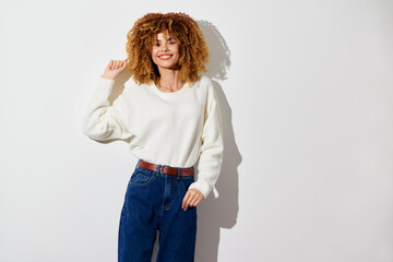 Wall Mural - happy woman with curly hair in casual white sweater and blue jeans, standing against a minimalistic white background, smiling warmly and radiating positivity