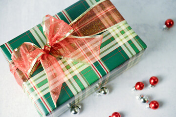 Festive plaid gift with glittery red bow surrounded by ornaments