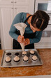 © Cavan - Female baker adding vanilla frosting a dozen chocolate cupcakes
