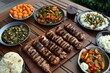 © Khawla - Middle eastern, arabic or mediterranean dinner table with grilled lamb kebab, chicken skewers with roasted vegetables and appetizers variety serving on wooden outdoor table. Overhead view