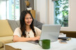 © Prathankarnpap - Cheerful young woman freelancer working with laptop on table in living room