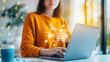 © Vilaysack - A woman in an orange sweater uses a laptop, with digital shopping icons displayed, suggesting online shopping or e-commerce activity.