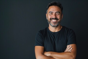 Happy Hispanic man in black shirt with crossed arms.