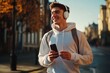 © vefimov - A young man wearing earbuds and smiling while walking down a street with his backpack.