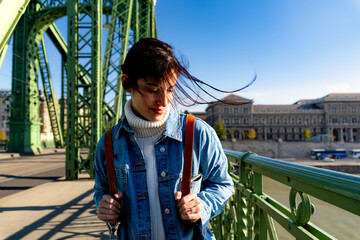 Wall Mural - A light smile on her face, a woman looks around with her head slightly down, her hair flowing in the breeze on the bridge 