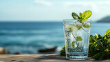 Orzeźwiająca szklanka wody z miętą na rustykalnym stole, na tle błękitnego morza i słonecznego wybrzeża.