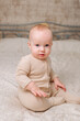© Katrin_Primak - Adorable happy healthy baby boy in beige overalls sitting on bed and smiling