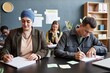 © Seventyfour - Medium shot of adult Muslim woman writing in exercise book sitting at desk with male fellow student writing test while studying English in language course group, copy space