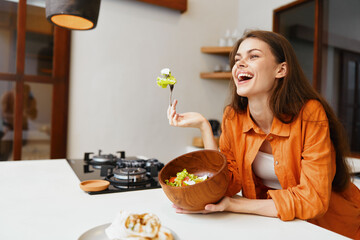 Canvas Print - Young woman enjoying a healthy salad in a cozy kitchen, smiling joyfully while holding a fork and a wooden bowl Fresh ingredients highlight a vibrant lifestyle