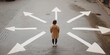 © laddawan - A solitary person stands at a crossroads of painted arrows on the ground, symbolizing the contemplation and choices of life's many directions and paths.