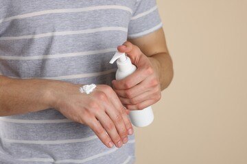 Wall Mural - Man applying hand cream from pump bottle on beige background, closeup. Space for text