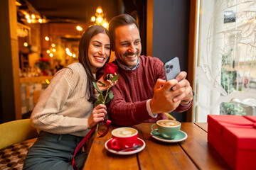 caucasian mid adult couple, dressed in stylish sweaters, takes a cheerful selfie in a cozy cafe with