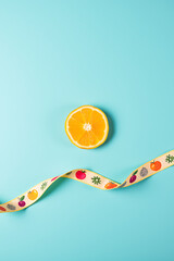 Poster - A small orange slice is placed on a large blue background next to a ribbon with colorful fruit patterns printed on it._00002_