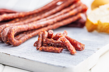 Wall Mural - Smoked kabanos. Mini dried thin sausages on cutting board on white table.