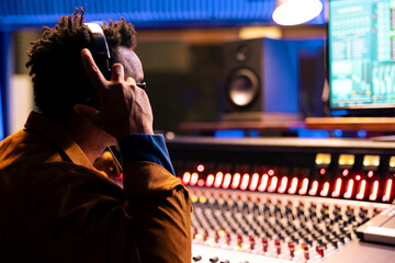Poster - Music producer using headphones when editing and processing tracks, recording in control room at professional studio. Audio engineer pressing buttons to add sound effects in post production.