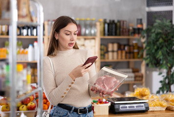 Wall Mural - Young female shopper scanning qr code for packaged raw pork meat in grocery store