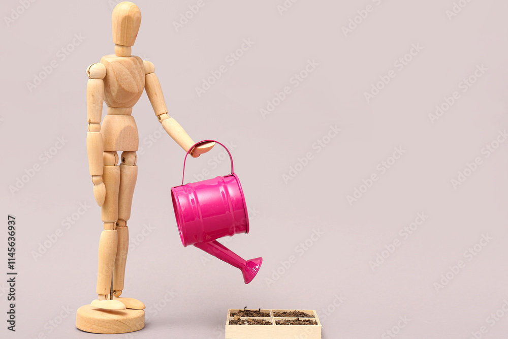 Wooden mannequin with pink watering can and box on grey background