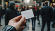 © Aditya - A hand holds a blank white card in front of a blurred city street background.  Perfect for showcasing your text or design.
