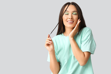 Wall Mural - Happy young Asian woman with stylish mint makeup on grey background