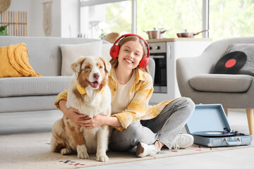 Wall Mural - Young woman in headphones with Australian Shepherd dog and record player at home