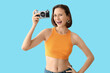 © Pixel-Shot - Pretty young woman with photo camera on blue background