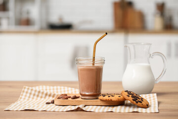 Glass of sweet chocolate milk with cocoa beans and tasty cookies on wooden table in kitchen