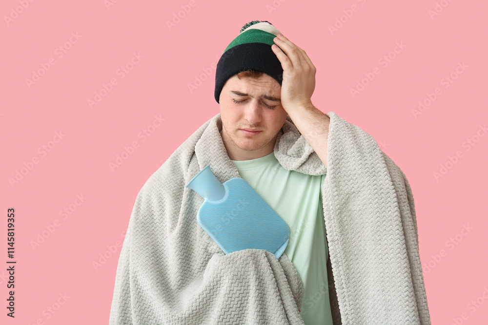 Ill young man with hot water bottle on pink background