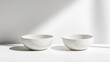 © siriporn - A pair of speckled white ceramic bowls resting side by side on a clean surface, surrounded by soft shadows.