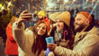 © master1305 - Cheerful group of friends smiling while capturing selfie during winter gathering outdoors, drinking hot drinks, enjoying the festive atmosphere. Concept of winter holidays, Christmas, traditions