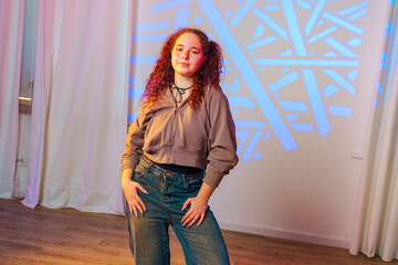 Poster - a young woman with red curly hair stands in front of a wall with a blue light projection