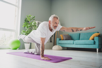 Wall Mural - Elderly man practicing yoga in bright living room, maintaining fitness and healthy lifestyle