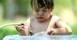 © Marco - Toddler boy playing with water hose outdoors during summer day inside bucket
