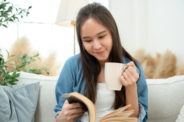 Wall Mural - Young Asian woman enjoying reading book in living room at home