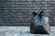 © Rekalawa - A black garbage bag placed on a paved surface against a textured wall.