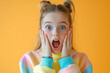 © Veronika - A teenage girl with her hands on her cheeks, her mouth open in awe, wearing a pastel-colored sweatshirt and a rainbow bracelet