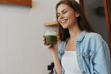 Canvas Print - Young woman enjoying fresh green juice in a cozy kitchen, embodying healthy lifestyle and vibrant energy with a bright smile and casual fashion