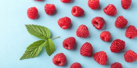 Poster - A vibrant arrangement of ripe red raspberries with a single green leaf on a blue background