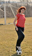 © aspenphoto - Beautiful young Caucasian woman with red hair standing with one foot on a soccer ball wearing a red mesh practice jersey