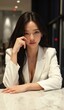 © Joedifries - A confident young Asian woman in a crisp white blazer, striking a relaxed pose at a marble table, her glowing skin emphasized by directional lighting, with realistic reflections on her face and hair