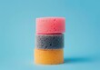 © SHOTPRIME STUDIO - colorful sponges stacked on a blue background, showcasing vibrant pink, gray, and yellow hues in a creative arrangement for cleaning or home decor uses