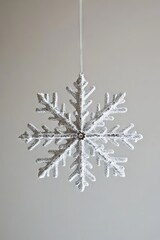 Wall Mural - A snowflake ornament hangs from a string. The snowflake is white and has a silver center