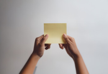 Aufkleber - A pair of hands hold a yellow sticky note in front of a plain white background.