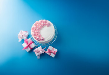 Aufkleber - A single-tiered white cake with pink frosting sits on a clear cake stand surrounded by three pink wrapped gifts. The cake and gifts are on a bright blue background.