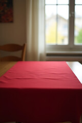 Poster - A red tablecloth is draped over a wooden table with a blurred view of the surrounding home through a nearby window._00001_