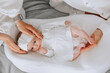 © Vasil - A baby is laying on a white blanket with a white dress on. A woman is holding the baby's head