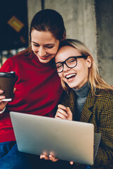 Fototapete - Portrait of happy blonde female blogger laughing at camera while having fun with best friend enjoying communication with each other and watching funny video on websites on laptop with 4G internet