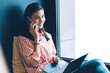 © BullRun - Young attractive positive female person communicating with friends in good atmosphere via modern smartphone.Pretty smiling woman talking on cellular while installing application on laptop computer