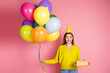 © deagreez - Excited young woman holding vibrant balloons and cake against a pink background